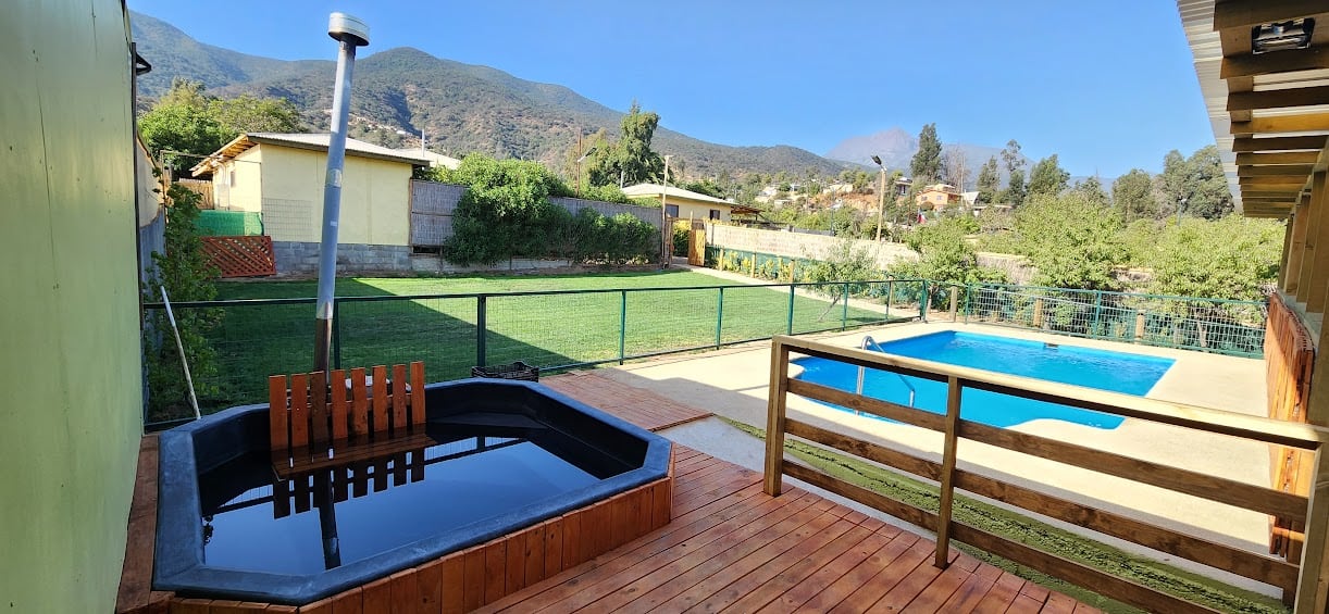 La terraza de madera de una casa, con su piscina y los cerros de Olmué al fondo