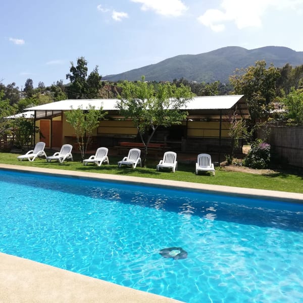 La piscina con las reposeras, el quincho al fondo y los cerros de Olmué