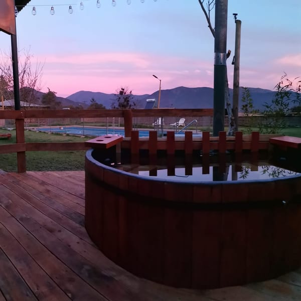 La tinaja de madera sobre el deck al atardecer, con la piscina detrás